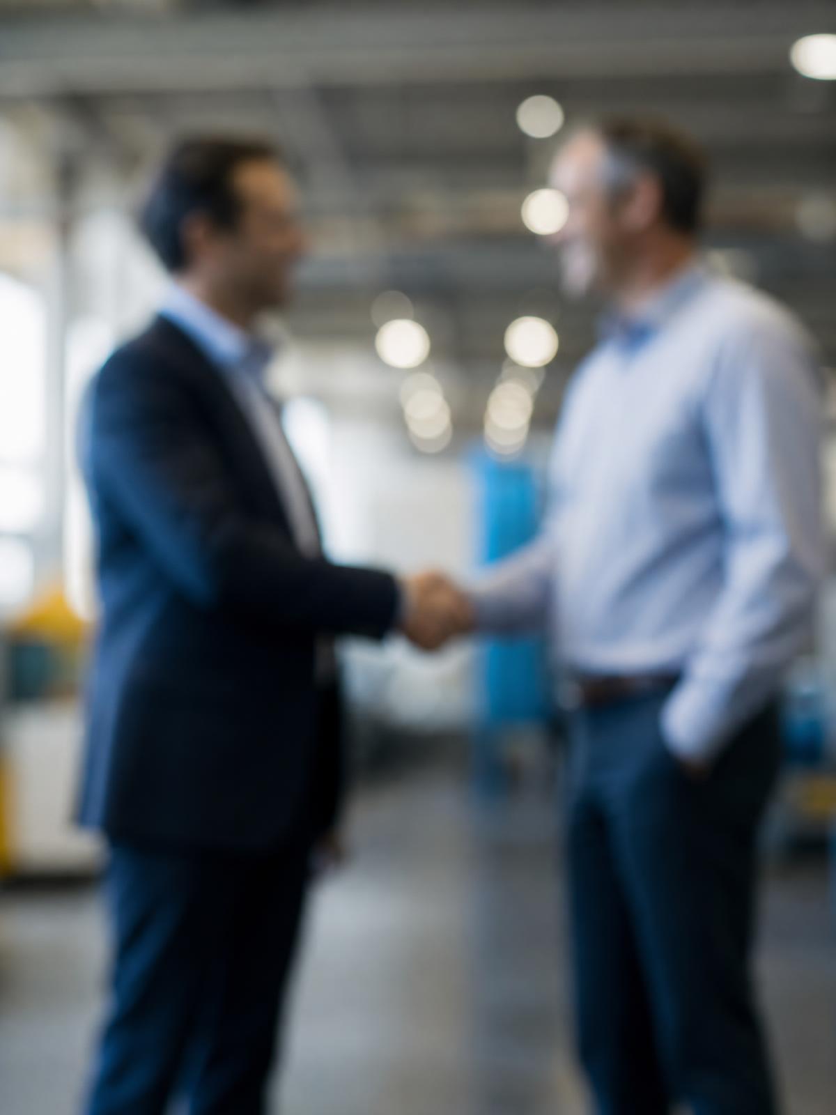 Handshake between a sales professional and a client in an industrial environment, blurred background